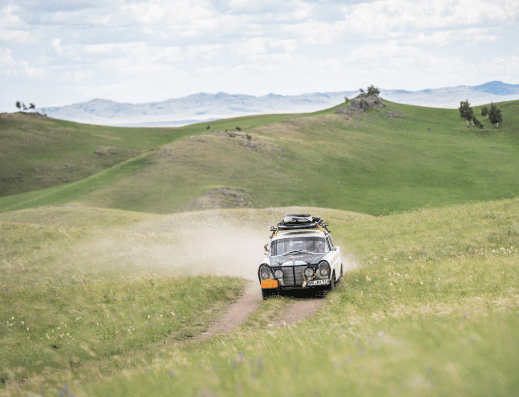 Groene heuvels met oldtimer op de route van de rally van Peking naar Parijs.