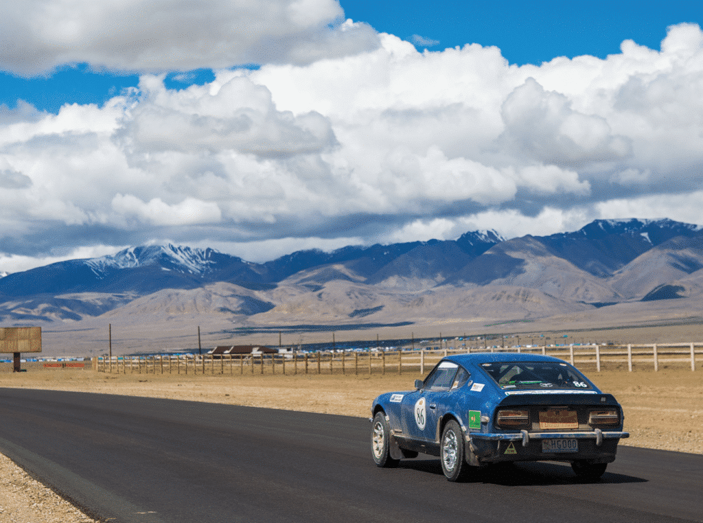 Blauwe oldtimer met bergen op de achtergrond. Auto van deelnemend team van de rally van Peking naar Parijs