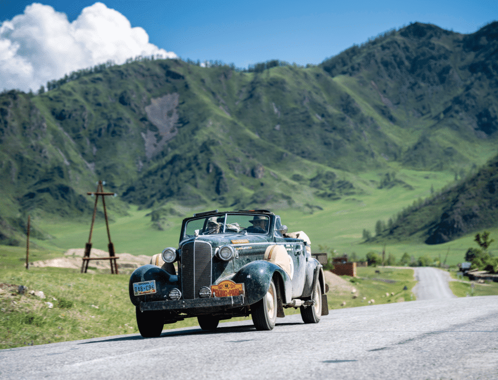 Foto van groen, bergachtig gebied en oldtimer op de voorgrond. Locatie is Altai Region tussen Mongolië, Rusland en Kazachstan, dat op de route ligt van Peking naar Parijs.