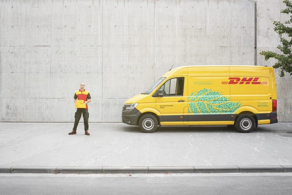 a male DHL courier next to an electric DHL van as part of our green DHL fleet