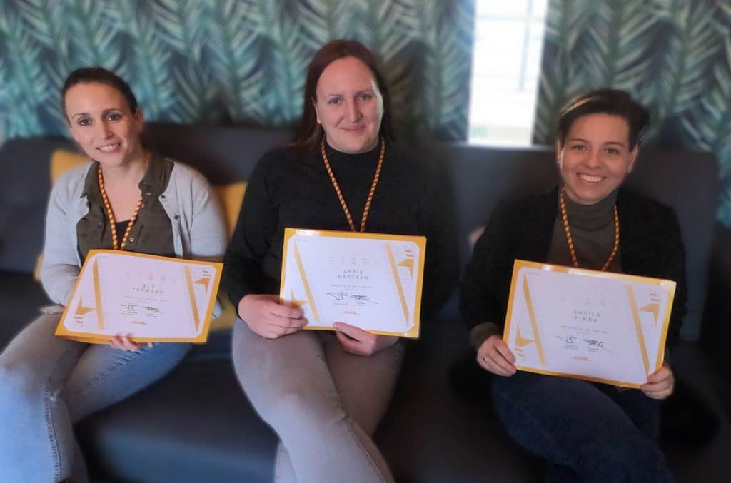 Three women sitting on a couch with their Employee of the Year certificates.